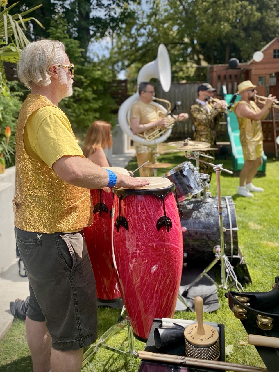 A man standing playing conga drums with other musicians in the band playing nearby
